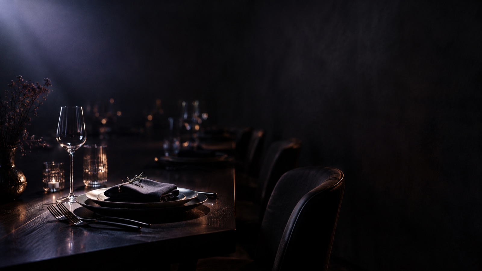 Ein langer gedeckter Tisch im Dunkeln, nur ein einziges Gedeck liegt im Licht